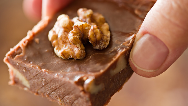 Hand holding fudge topped with walnut