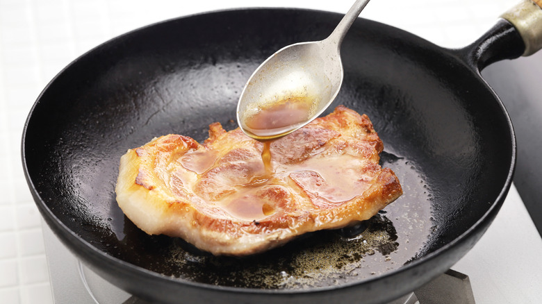 Spoon basting pork chop in pan