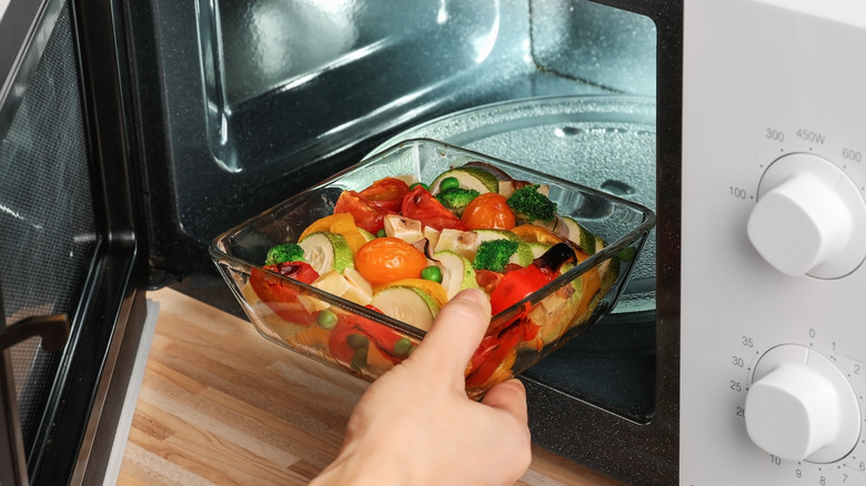 person placing vegetables into microwave