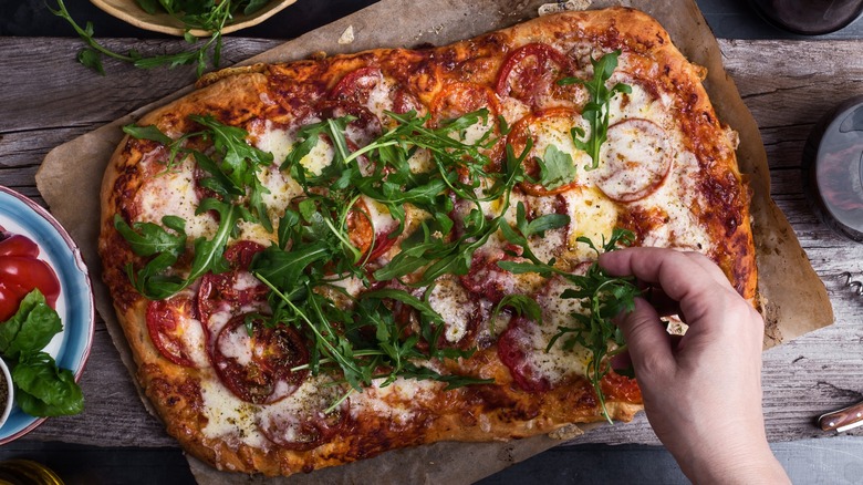 Hand sprinkling arugula on pizza