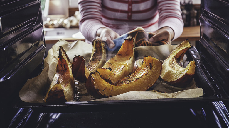 pulling roasted pumpkin on sheet tray out of the oven