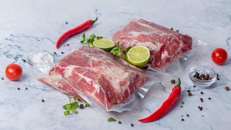 Two bags of sous vide pork next to peppers, limes, tomatoes, and peppercorns