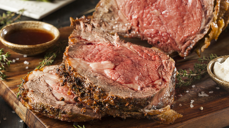 Slices of prime rib on a cutting board with a serving cup of au jus