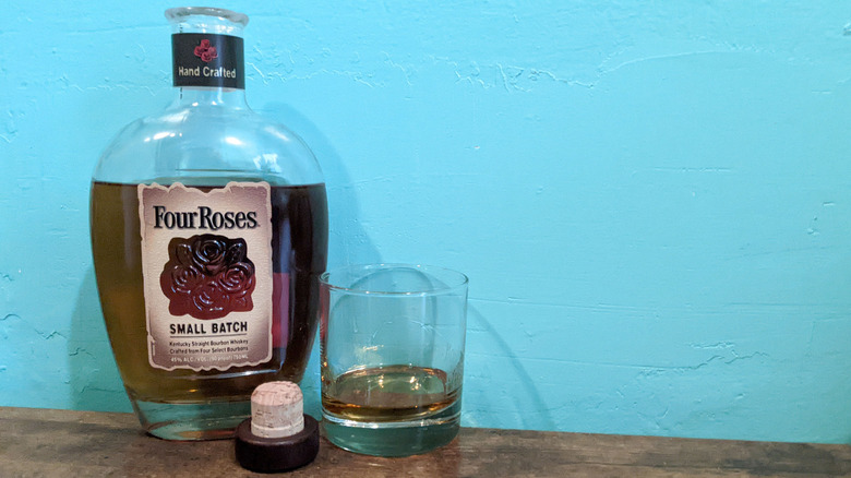 Four Roses Small Batch bourbon bottle uncorked next to rocks glass against blue wall