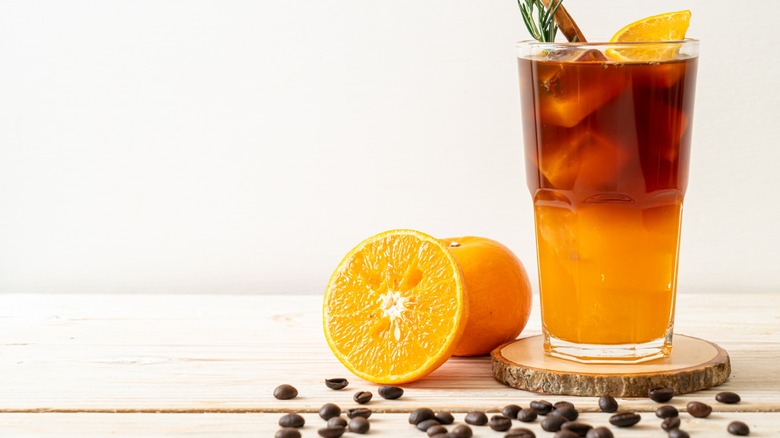 Glass of iced coffee next to sliced oranges and coffee beans