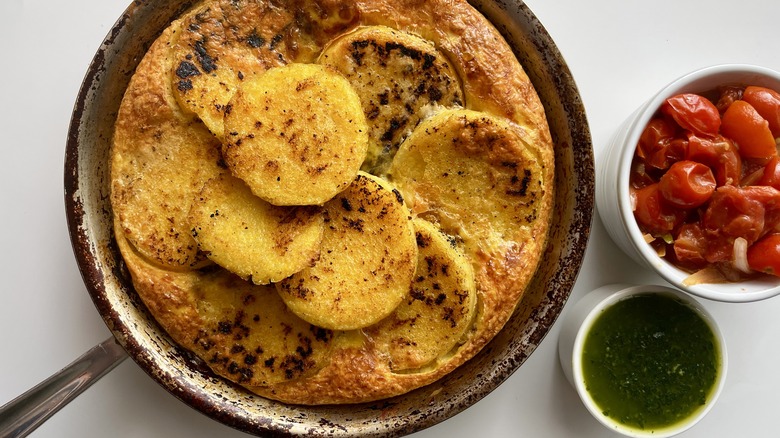 golden brown fried polenta frittata in a skillet with tomato sauce and pesto