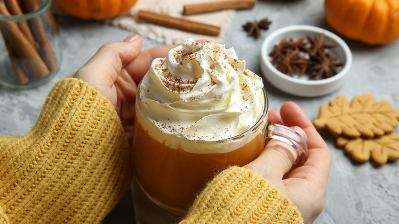 Hands holding latte with whipped cream