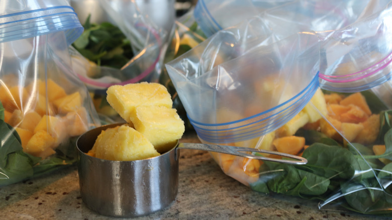 measuring cup with frozen pineapple with portioned smoothie bags in background