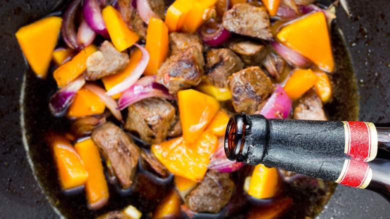 Bottle of alcohol being poured into meat stew