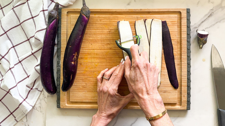 hands peeling eggplant on cutting board
