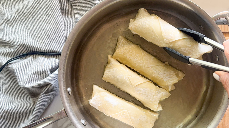 tongs adding eggroll to pan