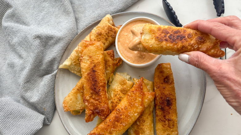 hand dipping eggroll in sauce