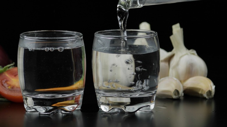 Vodka being poured into two glasses next to garlic cloves