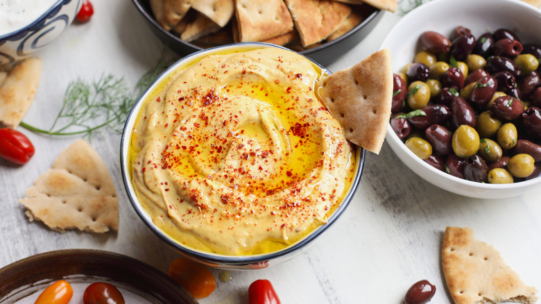 A bowl of hummus with bread and olives