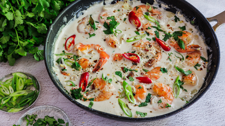 Shrimp in coconut milk in a pan with scallions and cilantro on the side