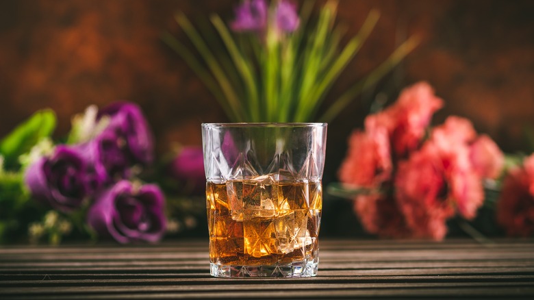 glass of whiskey with flowers in background