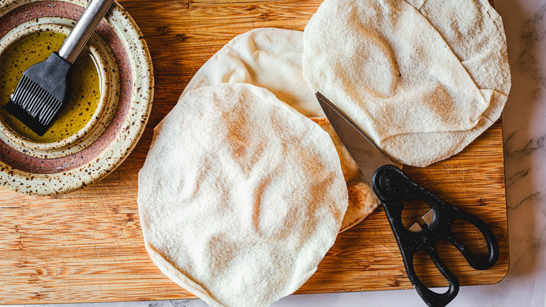 pitas and scissors and olive oil on cutting board