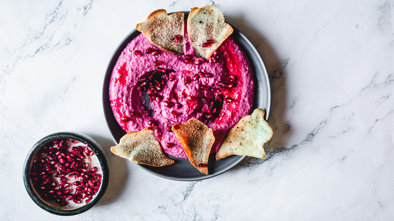 pomegranate seeds next to pink beet hummus and ghost shaped chips on black plate