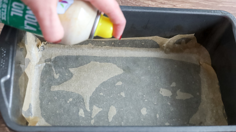 a loaf pan with parchment paper in the bottom being sprayed with nonstick spray