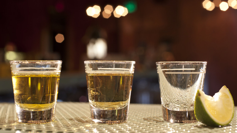 Three shot glasses of tequila next to lime slice