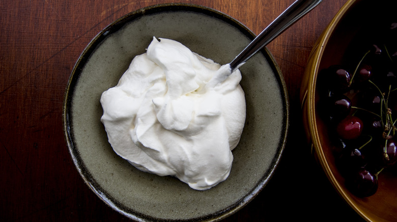 Bowl of whipped cream and spoon next to bowl of cherries