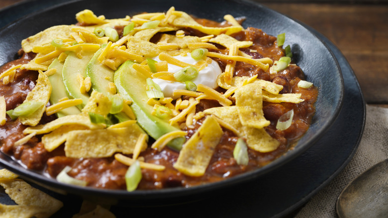 Chili dip topped with avocado, cheese, and corn chips