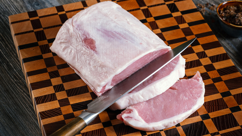 raw pork loin on a cutting board, being sliced with a kitchen knife