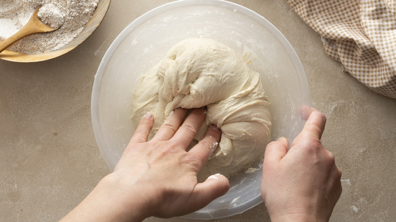 hands kneading sourdough in bowl 