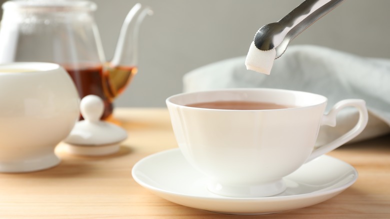 adding sugar cube to tea with tongs