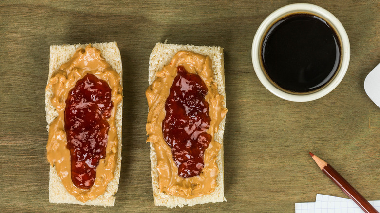 peanut butter and jelly spread on a sub roll next to a cup of coffee