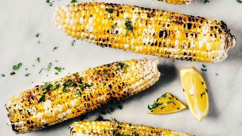 Two roasted corn cobs with lemon wedges and herbs