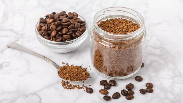 coffee beans in bowl and ground coffee in jar on white marble background