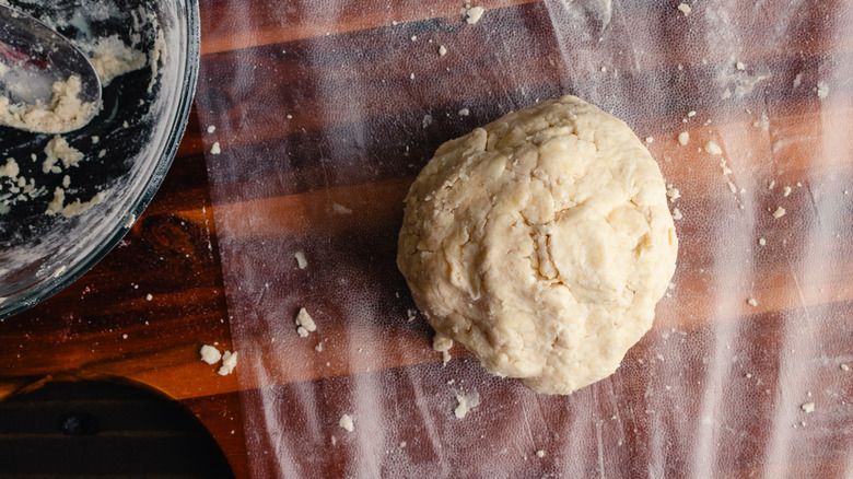 A ball of pie dough about to be wrapped next to an empty mixing bowl and spoon