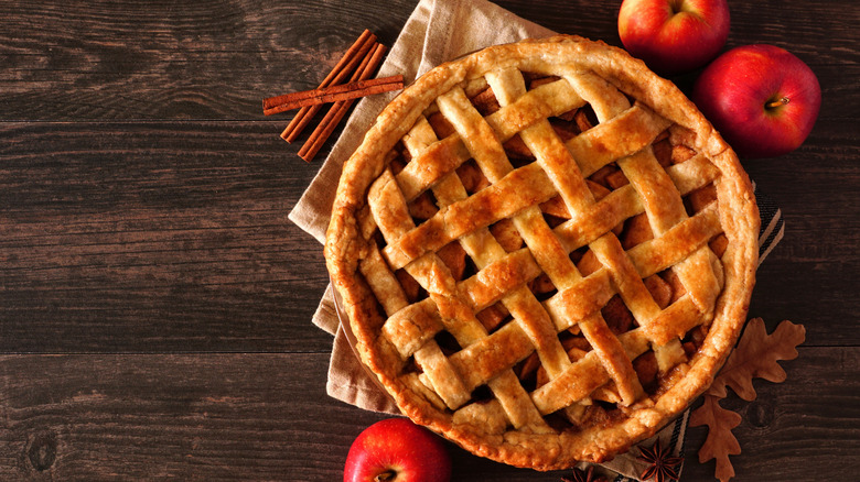 A latticed apple pie surrounded by apples