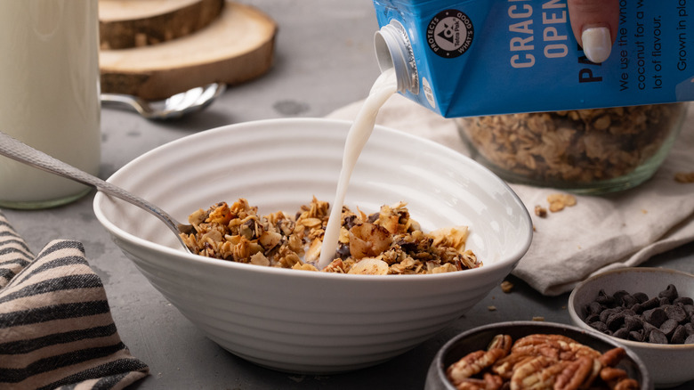 Hand pouring milk into white bowl of granola