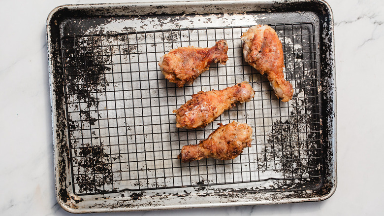 Fried drumsticks on cookie drying rack above baking sheet