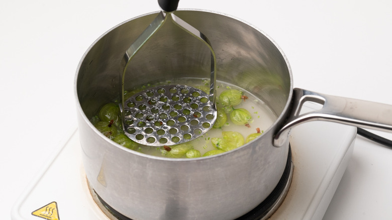 crushing gooseberries with potato masher