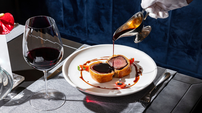 two slices of beef wellington on a plate with sauce being poured over