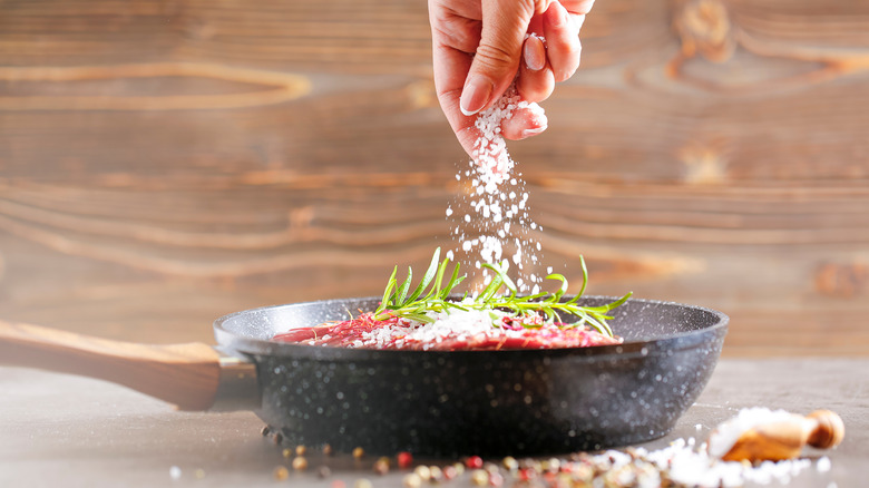 Hand seasoning steak in pan