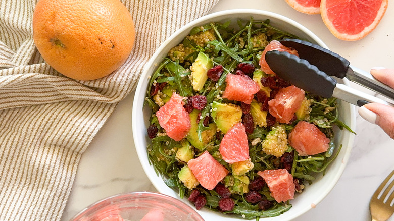 tongs adding grapefruit to salad