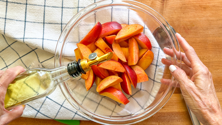 hand adding oil to bowl of nectarines