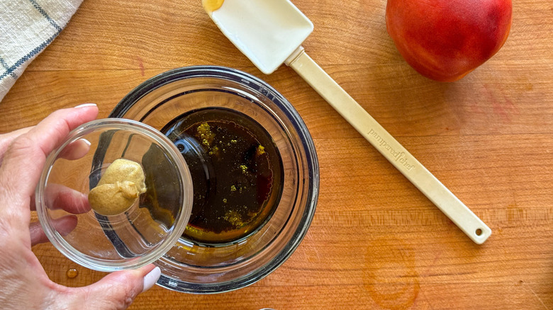 hand adding dijon to bowl of dressing