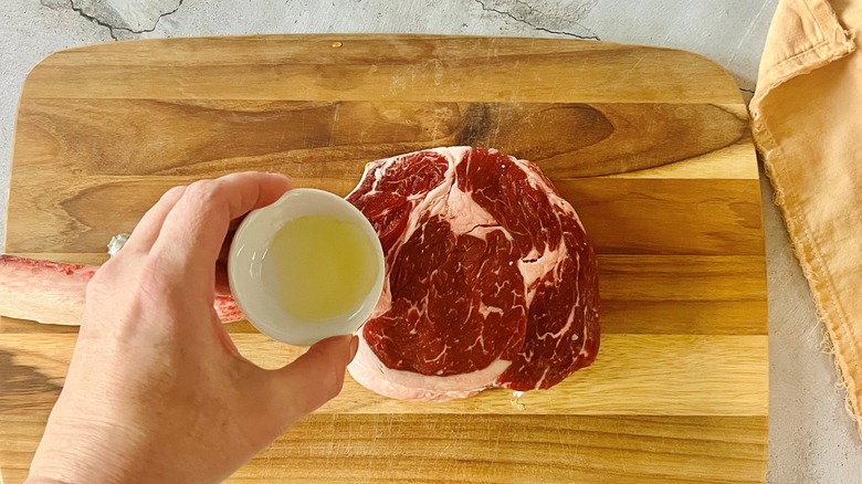 hand pouring oil on steak over cutting board