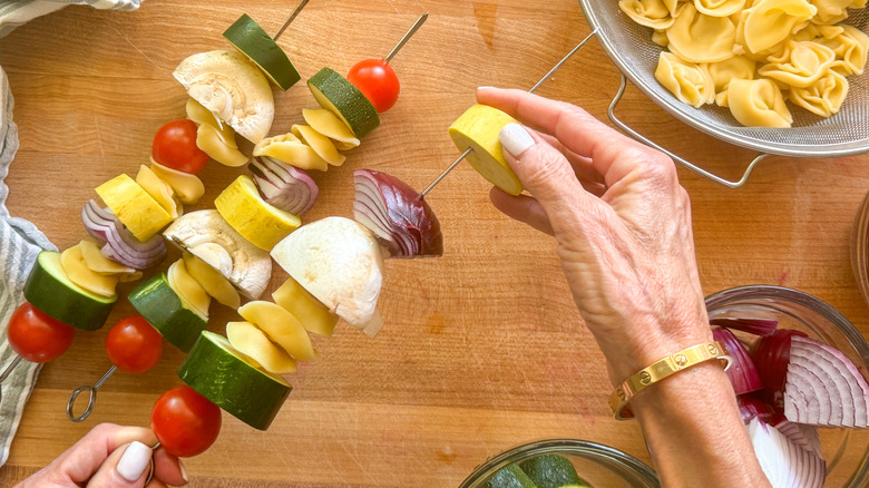 hand adding squash to skewer