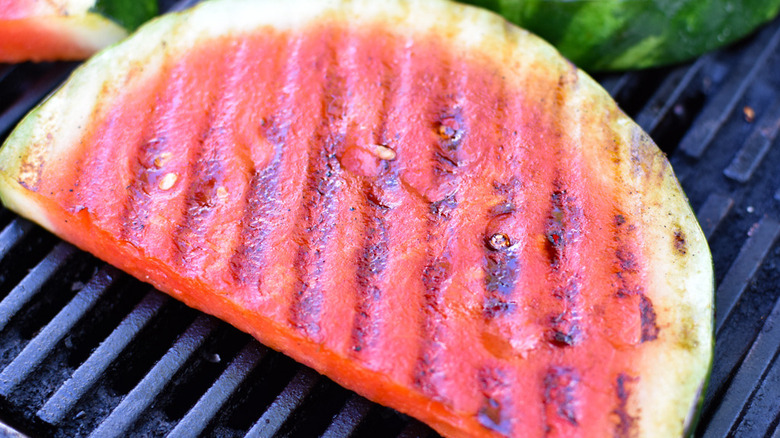 A slice of watermelon coated with olive oil and seasoned with salt and pepper cooking on a grill