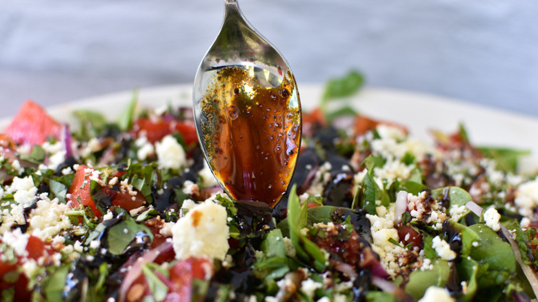 Close up of a metal spoon drizzling a balsamic dressing over a grilled watermelon salad