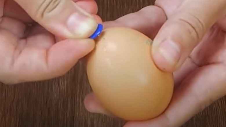 hands pushing tack into egg