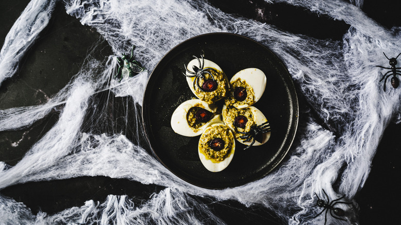 four deviled eggs with plastic spiders on black plate