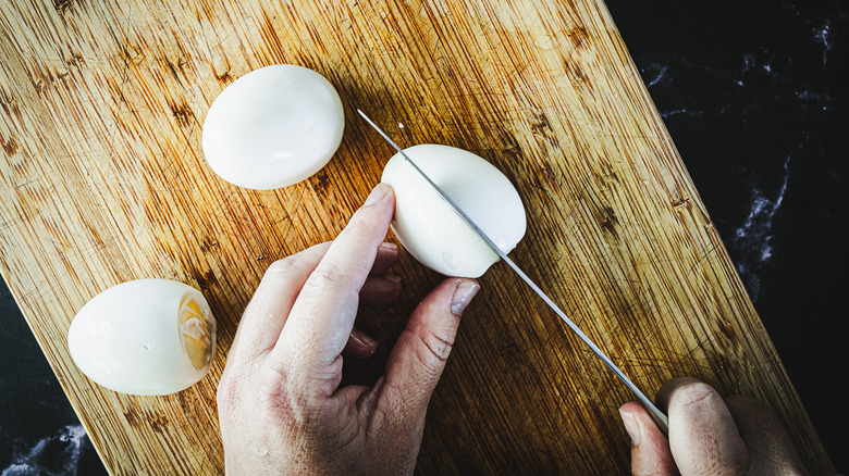 slicing an egg in half on cutting board