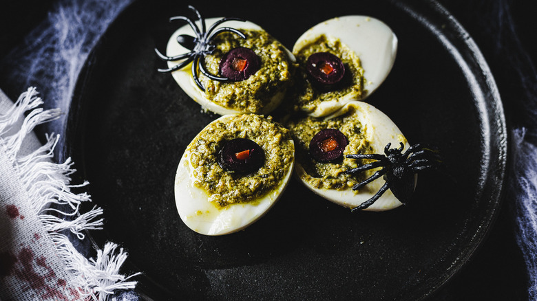 four deviled eggs with plastic spiders on black plate